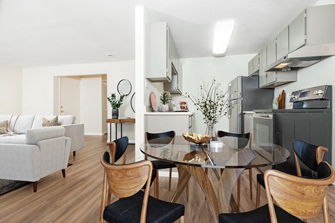 Dining area with glass table surrounded by chairs.  Kitchen and living room visible on either side at University Glen, University Place, WA